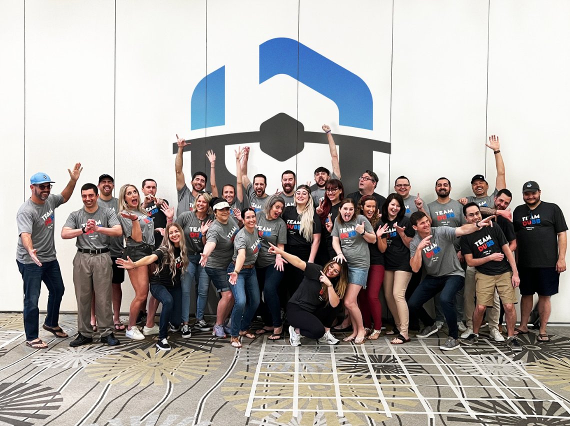 The whole BuyerBridge team celebrating together in front of the BuyerBridge logo